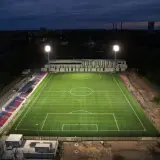 Piękny, oświetlony stadion Polonii Bytom nocą. Zielona murawa i czerwono-niebieskie trybuny czekają na kibiców.