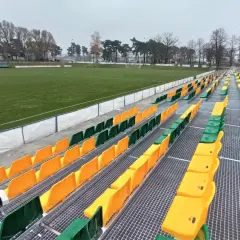 Puste trybuny stadionu Lechii Zielona Góra, z rzędami zielonych i żółtych krzesełek.