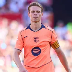 Frenkie de Jong w pomarańczowej koszulce FC Barcelony z opaską kapitana na ramieniu, skupiony na boisku.