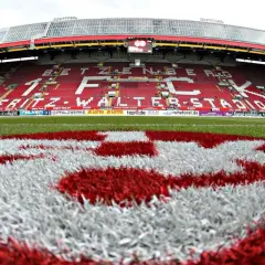 Na murawie stadionu Fritz-Walter-Stadion, symbol klubu FC Kaiserslautern. Czerwono-białe barwy drużyny dominują na trybunach i boisku.