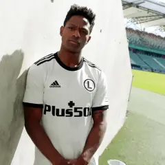 Joel Valencia w białej koszulce Legii Warszawa, z logo Plus500, na tle stadionu.