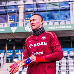 Bramkarz w bordowej koszulce z orłem, gotowy do gry. Gdzie gra Skorupski? Na stadionie, wśród pustych trybun.
