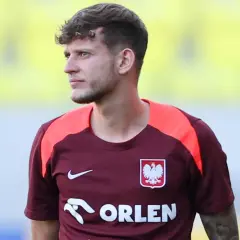 Piłkarz w bordowej koszulce z orłem, gdzie gra Szymański.