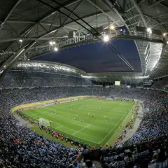 Widok z góry na pełny stadion Red Bull Arena Leipzig, gdzie tysiące kibiców w zielonych i niebieskich barwach dopingują swoje drużyny podczas nocnego meczu.