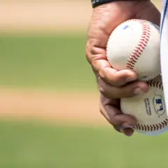 Dłoń trzyma dwie piłki baseballowe, gotowe do gry. Widać napis "EXTRA INNINGS TECHNOLOGY", świadczący o zaawansowanej technice niskiej piłki.