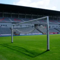 Pusta bramka na zielonej murawie stadionu KKS Kalisz. W tle trybuny i zadaszenie.
