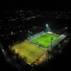 Nocne oświetlenie rozświetla zieloną murawę stadionu Sokoła w Ostródzie, otoczonego ciemnością i miejskimi światłami.