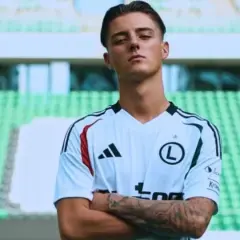Kacper Urbański, młody piłkarz w białej koszulce z czarnymi pasami, z dumą prezentuje swoje tatuaże.