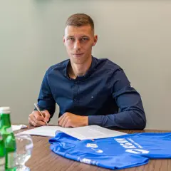 Dominik Hładun podpisuje kontrakt, obok leży niebieska koszulka.