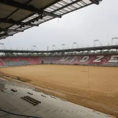 Trwa rozbudowa stadionu Widzewa. Na piaszczystym boisku widać prace budowlane i krzesełka w barwach klubu.
