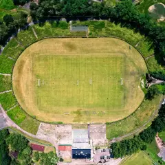 Widok z lotu ptaka na stadion Szombierki Bytom z zieloną murawą, trybunami i otaczającą go zielenią.