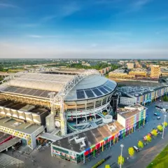 Johan Cruyff Arena, imponujący stadion z panelami słonecznymi na dachu, otoczony kolorowymi budynkami i zielenią.