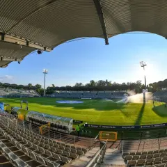 Pusta trybuna stadionu Miedzi Legnica, zielona murawa i zraszacze tworzą spokojny obraz przed meczem.