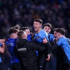 Radość zawodników po wygranym meczu w Pucharze Polski. Piłkarze w niebieskich strojach świętują zwycięstwo, otaczając jednego z kolegów.
