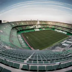 Puste trybuny stadionu Real Betis, zielone krzesełka tworzą mozaikę pod błękitnym niebem.