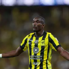 Piłkarz Moussa Diaby w żółto-czarnej koszulce z logo Iттihad Club, z otwartymi dłońmi, gotowy do gry.