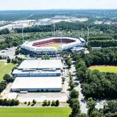 Widok z lotu ptaka na Max-Morlock-Stadion otoczony zielenią, z pobliskimi budynkami i boiskiem sportowym.