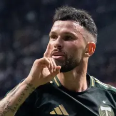 Piłkarz Kristoffer Velde w ciemnozielonej koszulce z złotymi paskami, gestykuluje palcem wskazującym do skroni.