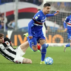 Piłkarze w akcji podczas rozgrywek Serie B. Jeden z zawodników w niebieskim stroju próbuje odebrać piłkę leżącemu na trawie przeciwnikowi w czarno-białej koszulce.