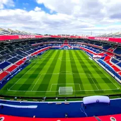 Pusta trybuna stadionu Parc des Princes, z czerwono-niebieskimi siedzeniami i zieloną murawą, gotowa na mecz Paris Saint-Germain.