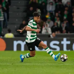 Piłkarz Sporting CP w zielono-białej koszulce drybluje z piłką na boisku.