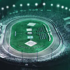 Nocny wyścig na stadionie Włókniarz Częstochowa. Tłumy kibiców na trybunach, oświetlony tor i zielona murawa.