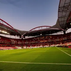 Pusta trybuna stadionu **Estadio da Luz** w Lizbonie, z zieloną murawą i czerwonymi siedzeniami.