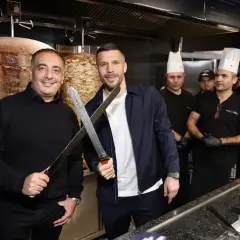 Lukas Podolski z nożami w ręku, obok niego pracownicy jego restauracji z kebabem.