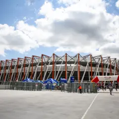 Nowoczesna chorten arena w Białymstoku, z charakterystyczną, ażurową konstrukcją dachu. Przed wejściem bramki obrotowe i łuk z logo stadionu.