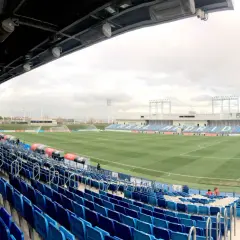 Puste trybuny stadionu Alfredo Di Stéfano, z zieloną murawą i niebieskimi siedzeniami, czekają na kibiców.