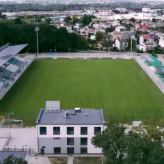 Stadion Wisłoki Dębica z zieloną murawą i trybunami, otoczony drzewami i zabudowaniami miejskimi.