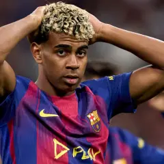 Młody piłkarz Lamine Yamal w koszulce FC Barcelona z blond lokami, trzymający się za głowę.