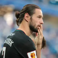 Grzegorz Krychowiak w czarnej koszulce, z włosami związanymi w kok, zamyślony na boisku.