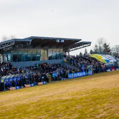 Widok na trybuny stadionu Avia Świdnik, wypełnione kibicami. W tle widać zadaszenie i drzewa.