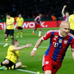 Piłkarz Bayernu w czerwono-niebieskiej koszulce cieszy się z bramki. W tle zawodnicy Borussii Dortmund w żółtych strojach.