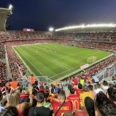 Widok z trybun na pełny stadion **Estadio La Rosaleda** podczas meczu piłki nożnej. Tłum kibiców w czerwonych barwach wypełnia trybuny.