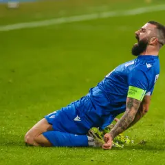 Mikael Ishak świętuje bramkę, klęcząc na zielonej murawie.
