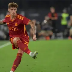 Nicola Zalewski w akcji, kopie piłkę na boisku w czerwonej koszulce AS Roma.