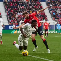 Piłkarze Real Madryt i Osasuna walczą o piłkę na murawie. W tle trybuny pełne kibiców.