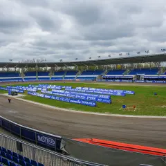 Pusty stadion żużlowy Orzeł Łódź z niebieskimi trybunami i torem żużlowym.