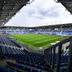 Puste trybuny stadionu Piasta Gliwice czekają na kibiców. Zielona murawa boiska lśni w blasku dnia.