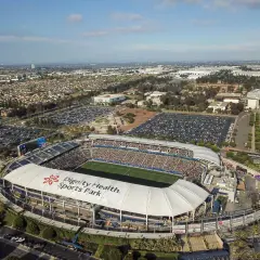 Widok z lotu ptaka na Dignity Health Sports Park, pełen widzów stadion piłkarski otoczony parkingami i miejską zabudową.
