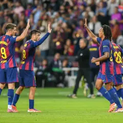 Piłkarze FC Barcelona świętują zwycięstwo w rozgrywkach. Lewandowski, Pedri i Koundé podnoszą ręce w geście radości na boisku.