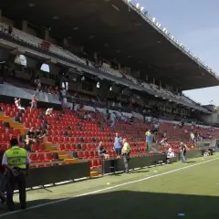 Puste trybuny stadionu Rayo Vallecano czekają na kibiców. Widać zieloną murawę i kilka osób na schodach.