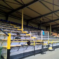Puste trybuny stadionu Gryf Wejherowo, z żółtymi i niebieskimi siedzeniami pod zadaszeniem.