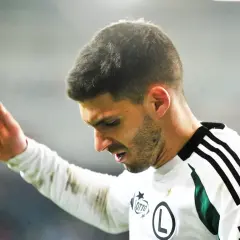 Piłkarz w białej koszulce z zielonymi wstawkami, z ręką uniesioną w geście. Czy to jego ostatni mecz w 4 lidze, zanim zarobki wzrosną?