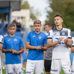 Pięciu młodych piłkarzy Hutnika Kraków w strojach klubowych stoi w rzędzie, klaszcząc.