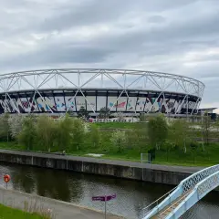 Ogromny stadion West Ham United z charakterystycznym logo klubu, otoczony zielenią i kanałem wodnym.