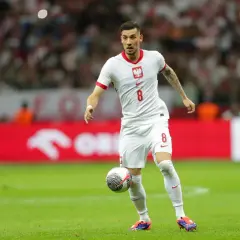 Jakub Moder w białej koszulce z numerem 8, z piłką przy nodze na boisku.