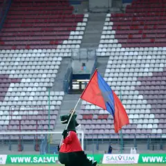 Maskotka Wisły Kraków z flagą na tle stadionu.